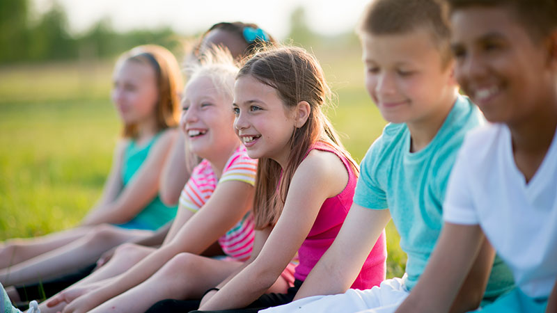 Lachende Kinder sitzen nebeneinander im Freien